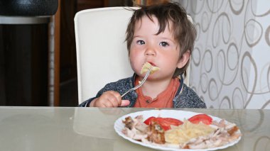 Çocuk masada çatalla makarna yiyor..