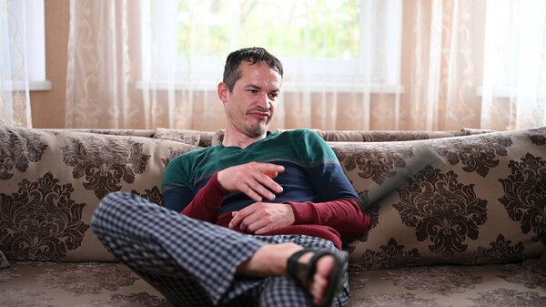 Displeased man sitting on a sofa with a TV remote.
