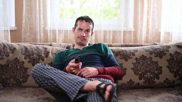 Displeased man sitting on a sofa with a TV remote.