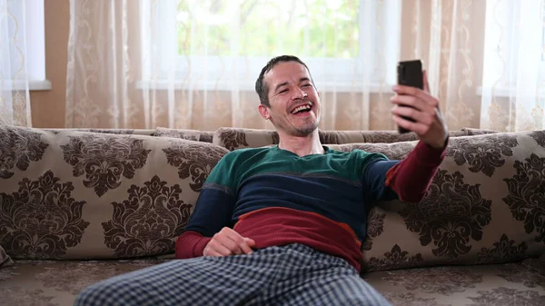 A man sits on a couch and talks through a mobile video call.
