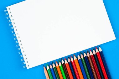 Gökkuşağı renginde kalemler ve mavi arka planda defterler. Okula geri dön, çizim yap. Minimalizm, düz yatış, telif alanı, üst görünüm