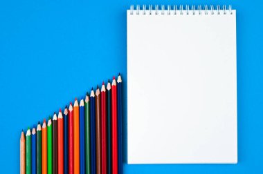 Gökkuşağı renginde kalemler ve mavi arka planda defterler. Okula geri dön, çizim yap. Minimalizm, düz yatış, telif alanı, üst görünüm