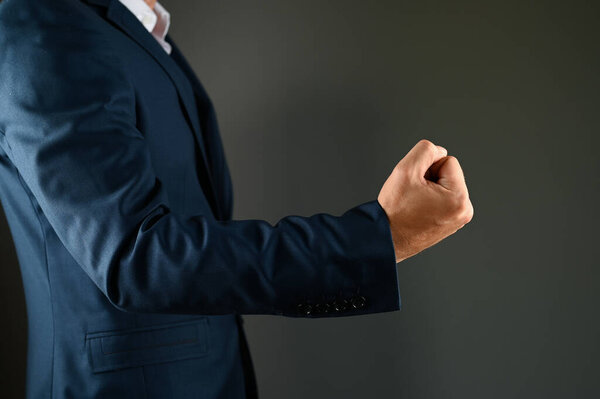 A man holds a fist in front. A man in a suit shows a kuak forward on a black background. Concept: strength in business. High quality photo