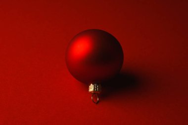 Kırmızı Noel topu gölgeli kırmızı bir yüzeyde yatıyor.