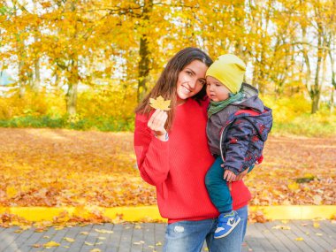 Parkta düşmüş sarı yaprakların arkasında çocuklu genç bir kız.