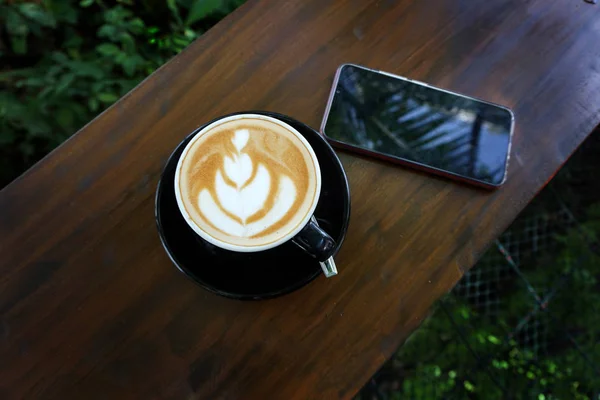 Šálek kávy s krásným Latte art na dřevěného stolku vedle mobilu — Stock fotografie