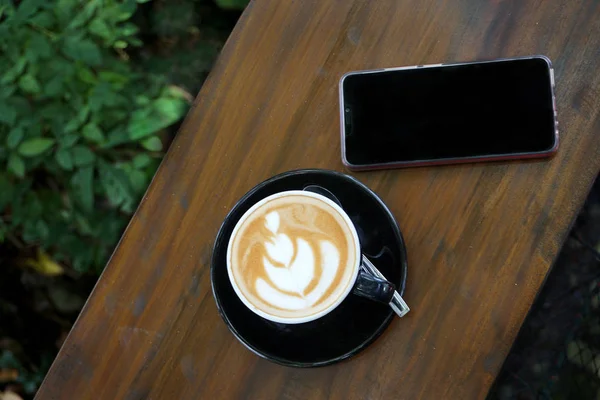 一杯咖啡与美丽的拿铁艺术在木吧桌旁边的手机 — 图库照片