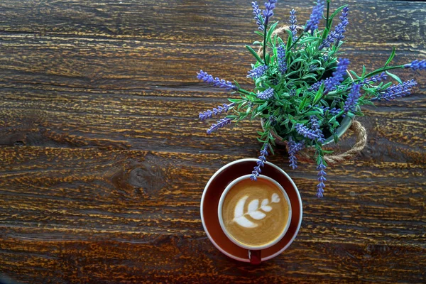 Šálek kávy s nádhernou latte a květinou na dřevěném stole — Stock fotografie