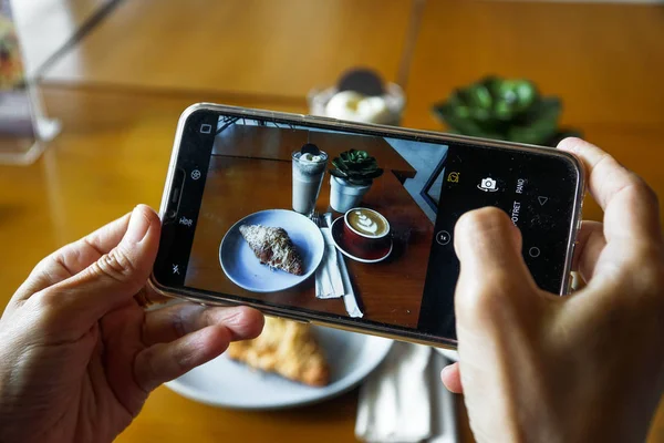 Cep telefonu kullanarak gıda fotoğrafçılığı. Kahve latte, kruvasan çikolata ve mavi okyanus ürün fotoğrafları. Sosyal medyada yüklenecek bir kafede en iyi görünüm fotoğrafı Stok Resim