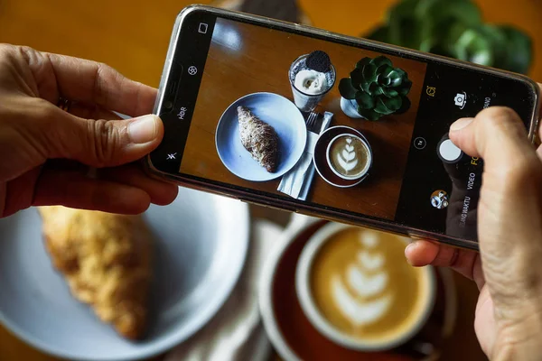 Cep telefonu kullanarak gıda fotoğrafçılığı. Kahve latte, kruvasan çikolata ve mavi okyanus ürün fotoğrafları. Sosyal medyada yüklenecek bir kafede en iyi görünüm fotoğrafı Telifsiz Stok Imajlar