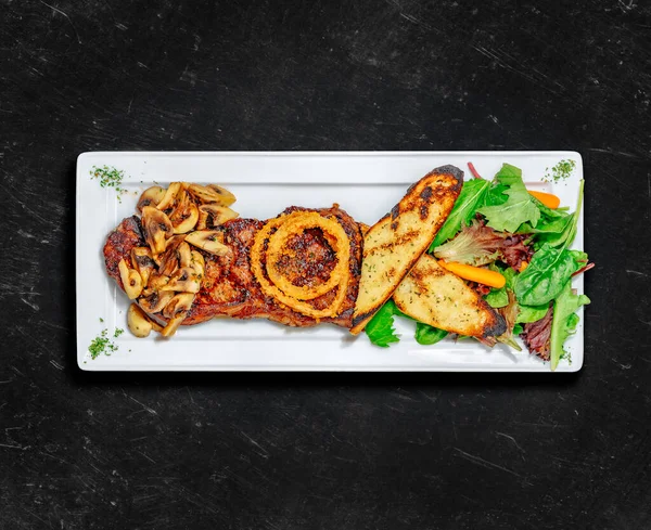 New York Striploin bifteği. Sağlıklı yiyecekler. İki taraflı ızgara biftek, sarımsaklı tost, mantar ve karışık salata. Kalıplaşmış. Üst görünüm