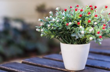 Tahta ahşap masa üzerinde beyaz seramik saksı dekoratif çiçekler, bulanıklık arka plan.