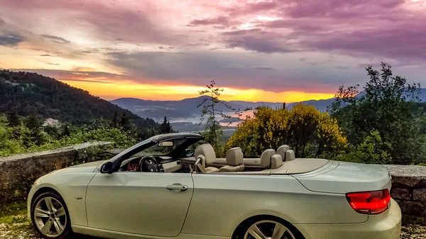Lyxig vit cabriolet på bakgrunden av solnedgången himlen i bergen. Royaltyfria Stockbilder