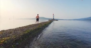 Taze deniz dalgaları üzerinde uçan düşük. Sabahın erken saatlerinde tükürük Tokarevsky deniz feneri doğru boyunca çalışan bir sporcu hava görünümünü. Güneş doğuyor. Vladivostok, Rusya Federasyonu