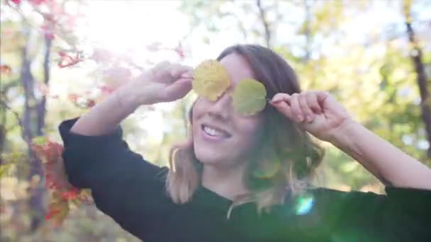きれいな女性 カメラに笑顔と葉を楽しんでの肖像画をスライドします 秋の公園 美しい日光 — ストック動画