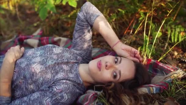 在秋林里 可爱的年轻女子躺在毯子上看着镜头的滑行景象 — 图库视频影像