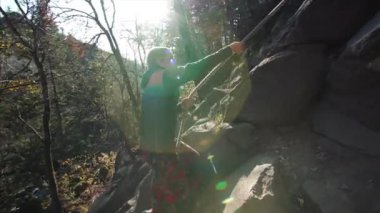 Bir adam halatla kayalık tepeye ya da dağa tırmanıyor. Sonbahar ormanı, güneşli hava