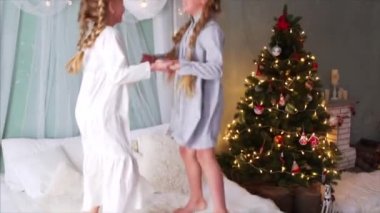 Saçları örgülü ve gecelikli iki mutlu kızın el ele tutuşması, yatağa atlaması, gülmesi ve Noel zamanının tadını çıkarması.
