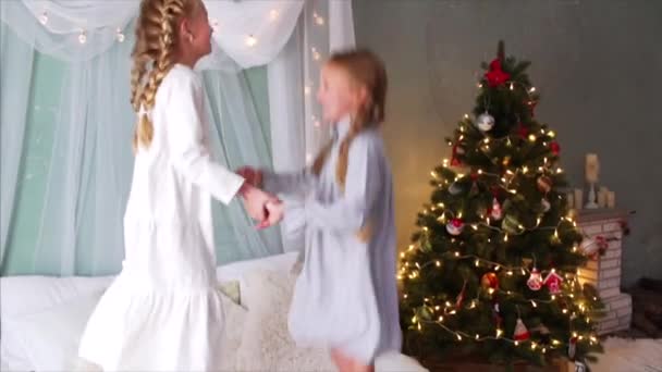 Lassú mozgás két boldog lány fonással és hálóingben fogja egymás kezét, ugrál az ágyon, nevet és élvezi a karácsonyt