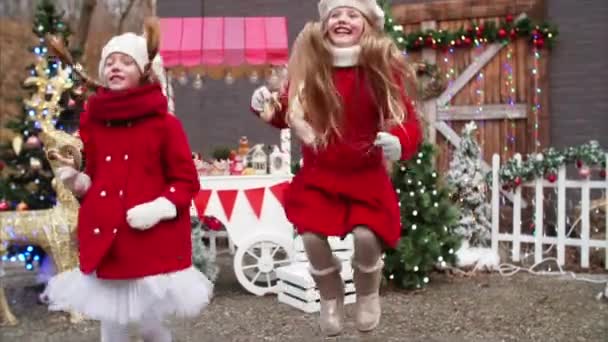 スローモーションビューの二つのかわいいです笑顔女の子で赤コートありますジャンプ高いです間でクリスマスフェア装飾 — ストック動画