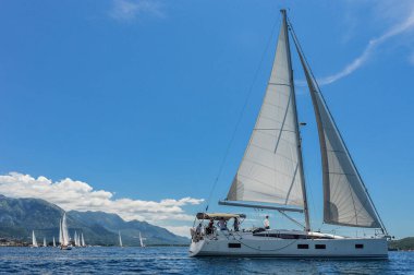 Güneşli bir yaz gününde bir köyle Adriyatik Denizi 'nin arka planında yelkenli ve yelkenli tekneleri. Denizde yelkenli yarışı.