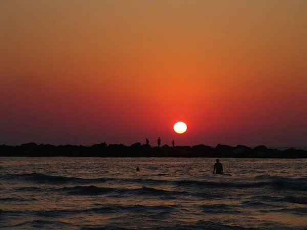 Günbatımında Bir Kayalık Pier Sahilde Duran Insan Siluetleri — Stok fotoğraf