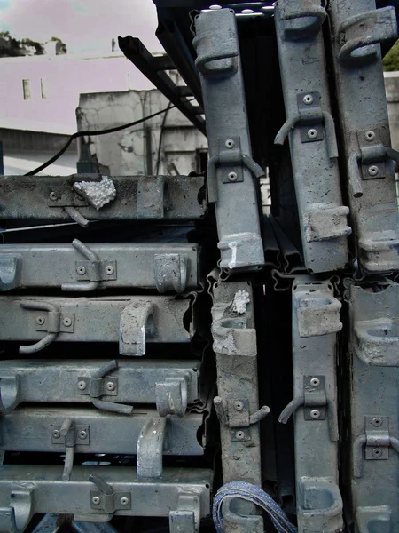 Stack of metal pieces, placed densely, at an urban building site at daylight, in black and white.