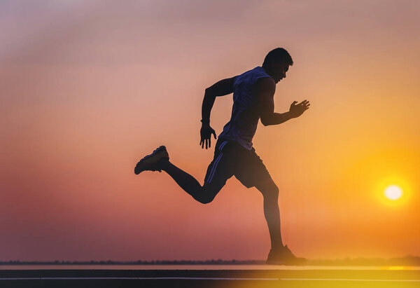 Silhouette of man running sprinting on road. Fit male fitness runner during outdoor workout with sunset background