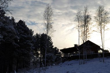 Kışın batan güneşin ışınları karlı orman arasında bir tepeüzerinde evin görünümü. Rus uzak yer.renkler beyaz, gri, mavi, yeşil