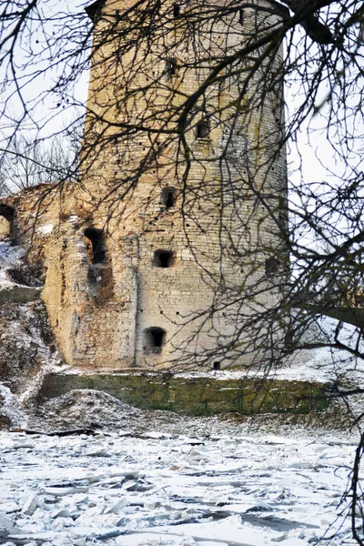 Kışın nehir tarafından dalları ile antik yıkık kuledikey foto, Rusya, Pskov. Krom eski duvarın bir parçası. Bir ağacın dalları odak dışındadır. renkler beyaz, sarı, gri, kahverengi.