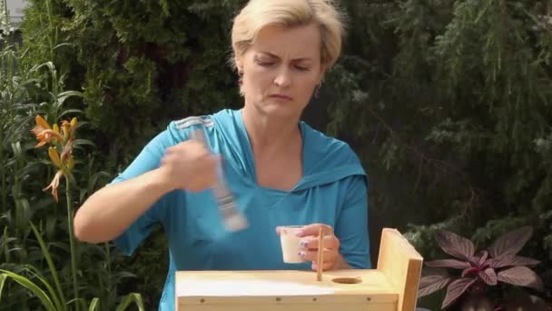 Красива жінка, що малює пташиний будинок білою фарбою — стокове відео