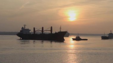 Rıhtıma gitmek için büyük bir kargo gemisini demirleyen bir römorkör. Limanın limanında bir kargo gemisi, bir mavna ve bir römorkör birbirlerine doğru yol alıyorlar. Akşam vakti. Gün batımı