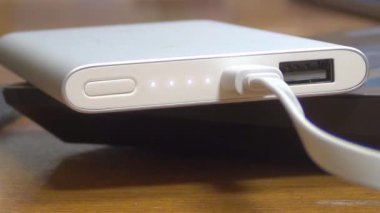 Güç bankası masada, şarj oluyor, ampuller yanıp sönüyor, beyaz kablo bağlanıyor, yakın plan, ahşap masa.