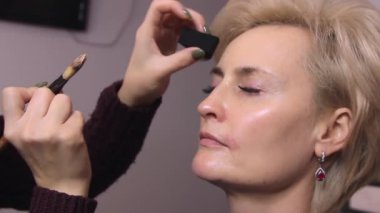 Makyaj sanatçısı fırça ve tamponla güzellik salonunda beyaz saçlı güzel bir mankenin yüzüne temeli atıyor.