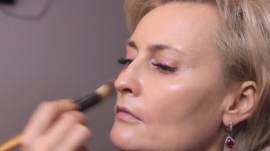 Makyaj sanatçısı fırça ve tamponla güzellik salonunda beyaz saçlı güzel bir mankenin yüzüne temeli atıyor.