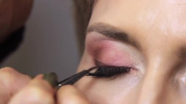 Bir güzellik salonunda, profesyonel bir makyöz, fırçalı bir kızın göz kapağına ince siyah bir çizgi çizer. yakın plan