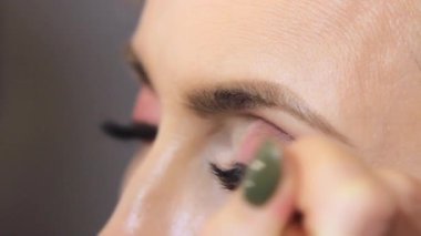 Bir güzellik salonunda, profesyonel bir makyöz, fırçalı bir kızın göz kapağına ince siyah bir çizgi çizer. yakın plan