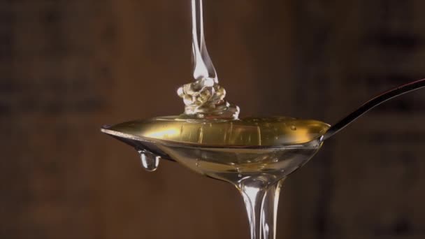 Honey dripping from the stainless tea spoon on wood background — Stock Video
