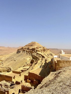 Dolambaçlı yol Tataouine 'deki troglodit köyü Qirmish' e çıkıyor, açık mavi gökyüzü altında toprak tonları ve çöl manzarasıyla karakterize ediliyor, tarihi konutlarını keşfetmeye davet ediyor..