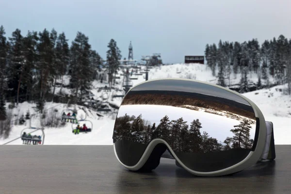 ski goggles on a wooden table with a reflection of the landscape from the top of the slope of the ski resort