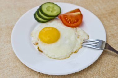 sağlıklı kahvaltı. Sahanda yumurta, dilim domates ve salatalık mutfak masasının üzerinde beyaz bir plaka üzerinde