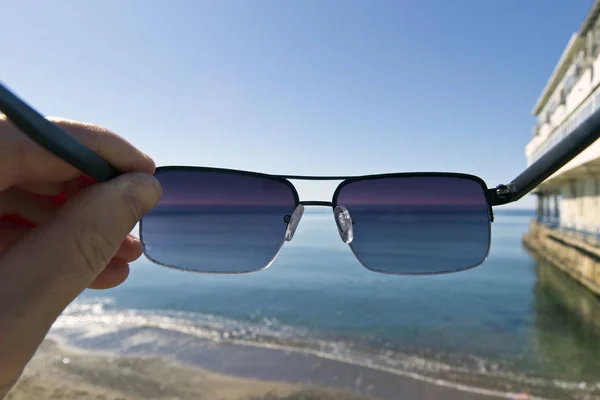 Bir adam sahil üzerinde duran güneş gözlüğü koyar. Birinci şahıs bakış