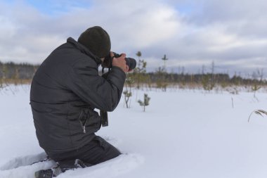 Karda oturan ağır bir fotoğrafçı bir kış manzara anlık görüntüsünü alır