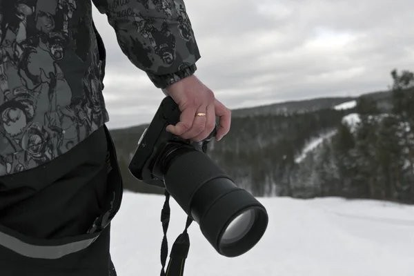 SLR camera with a long-focus lens in the hand of the photographer on the top of the mountain in winter