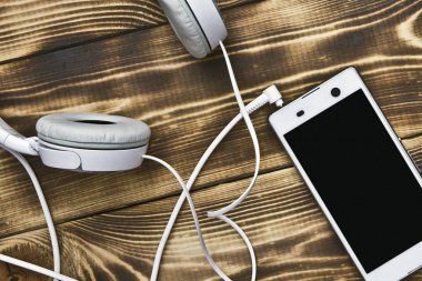 Ahşap bir masaya bağlı kulaklıklı beyaz akıllı telefon.
