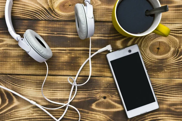 bir akıllı telefona bağlı kulaklıklar ve bir fincan sıcak kahve