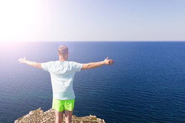 Deniz de bir dağın tepesinde duran genç bir adamın arka görünümü