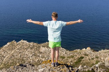Deniz de bir dağın tepesinde duran genç bir adamın arka görünümü