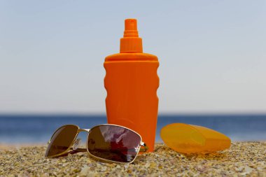 Kumsalda güneş kremi şişesi ve güneş gözlüğü