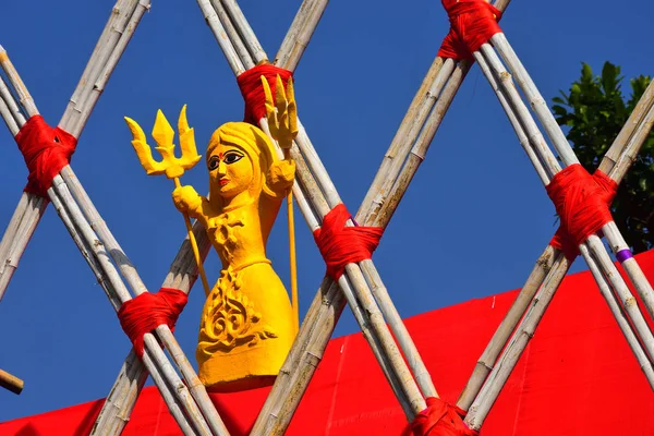 Poupée en argile de couleur jaune sur une structure parallélogramme de bâtons de bois attachés avec des cordes rouges et un fond rouge . — Photo